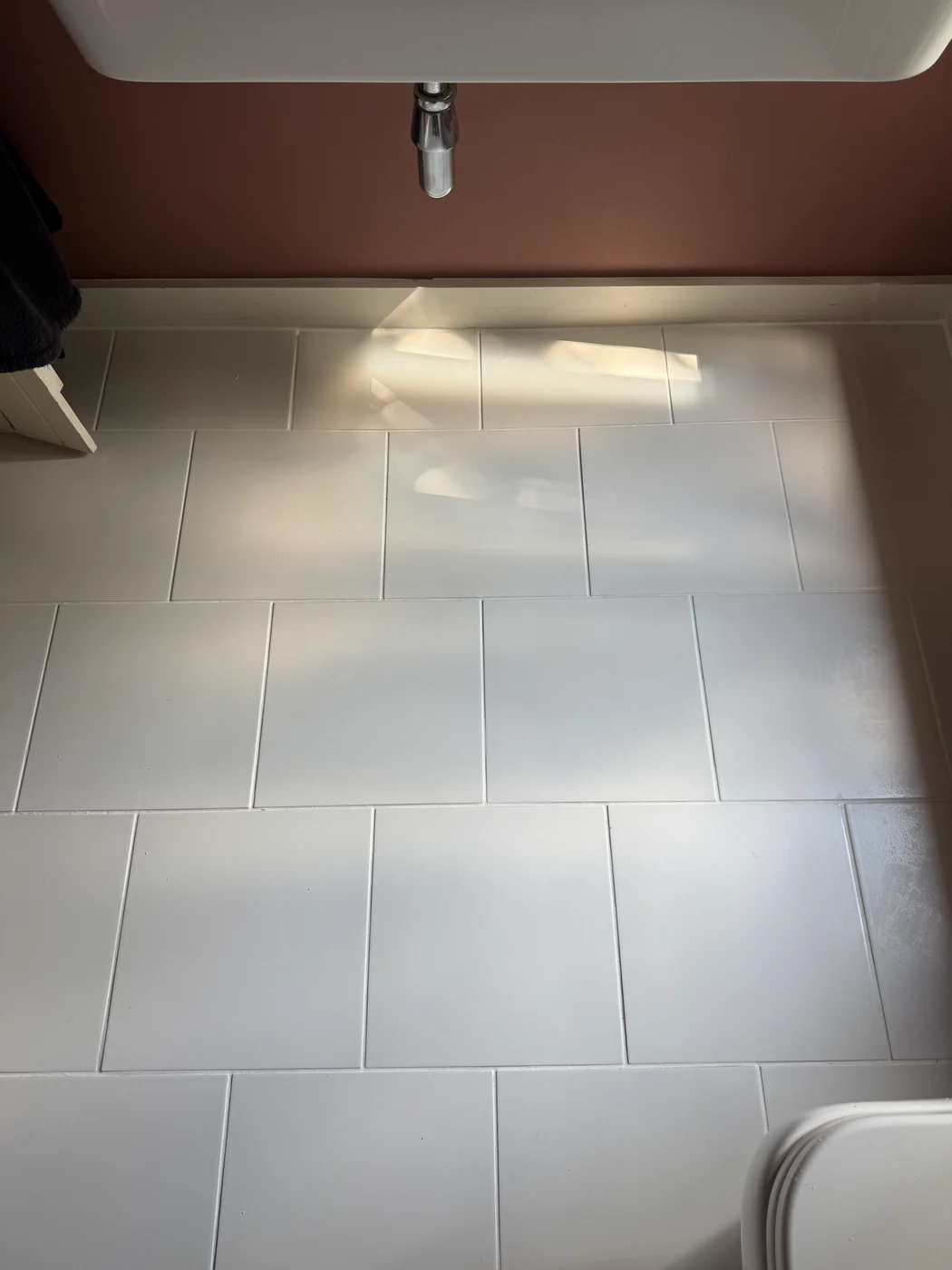 White bathroom floor tiles after restoration, viewed beneath the basin